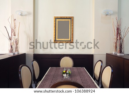 Just one corner of a restaurant, empty table and chairs with empty frame on the wall.