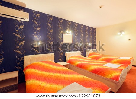 Interior of a hotel room for three persons, blue wallpapers and orange sheets on beds.