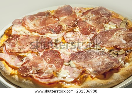 Pizza with meat and ham, served on white plate.
