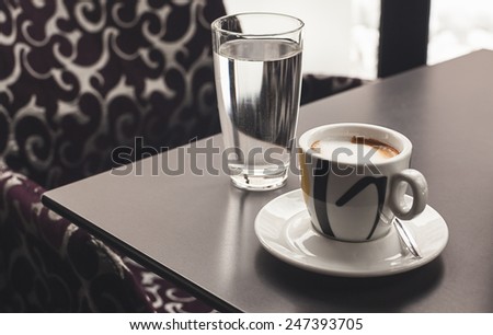 Cup of coffee and glass of water on table in a cafe.