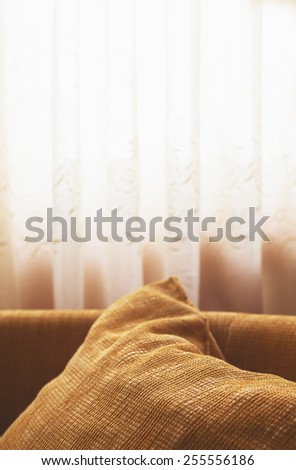 Just a detail behind the window, bedroom interior, big brown pillow in front and white curtains in background.