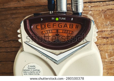 Details of an old guitar tuner, solid built with dust on surface, turned on.