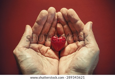 Two male hands holding red wooden heart, conceptual composition about love.