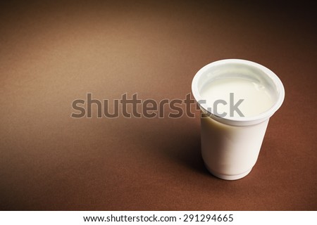 One glass of yogurt on right side, empty left brown background.