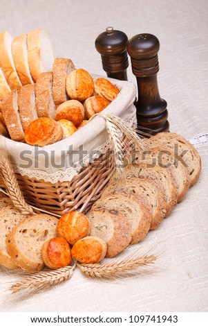 Assorted bakery products sliced, arranged in small basket. Wheat ears in front, salt and pepper behind