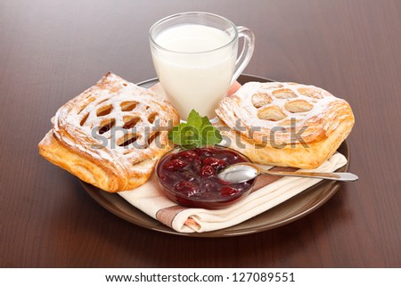 Sour cherry cake, jam and milk on plate, brown wooden background