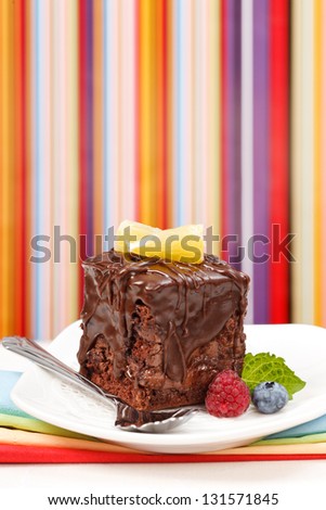 Cake with a chocolate gloss garnished with berries in front of colorful striped background - copy space above
