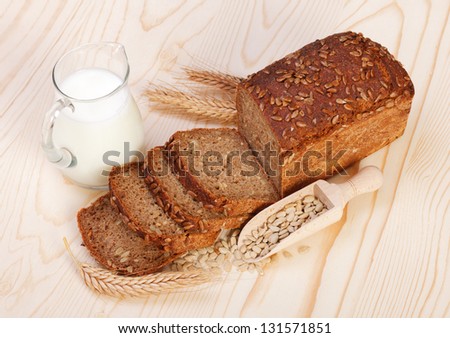 Brown sliced bread with seeds and jug of milk on wooden board