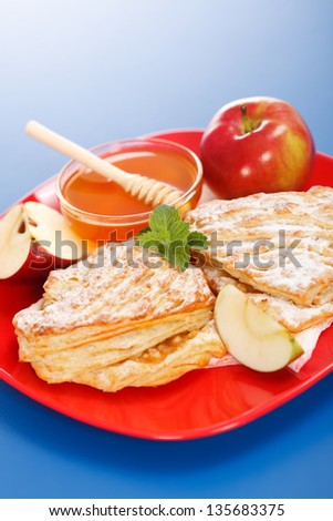 Apple cakes on plate, honey and apple pieces around, blue background