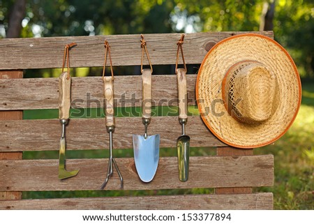 Garden tools and straw hat on board fence in garden