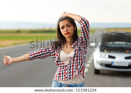 Sad woman hitch-hiking on the road in front of her broken car
