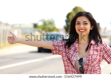 Pretty smiling lady hitch-hiking in the wayside