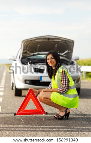 Woman wearing traffic suit, placing emergency triangle in front of a broken car