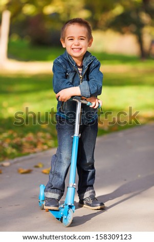 Smiling little kid with his kick scooter in a park