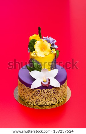 Colorful purple-yellow cake decorated with edible candy flowers and lace