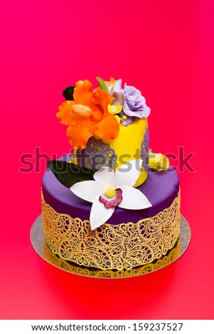 Colorful purple-yellow cake decorated with edible candy flowers and lace