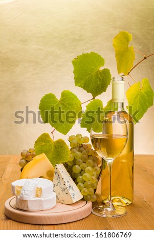 White wine in bottle and glass with grapes, camembert, emmentaler and blue cheese snack, grape leaves decoration