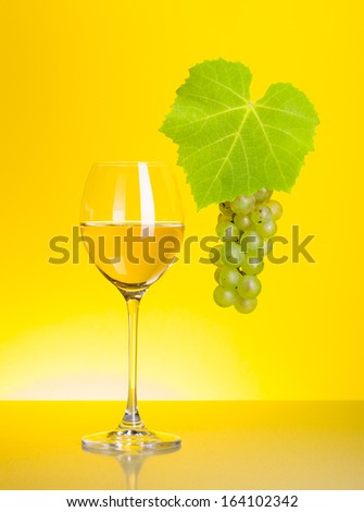 Glass of white wine with grape cluster on yellow background