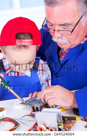 Grandfather teaching grandchild soldering of PCB with iron