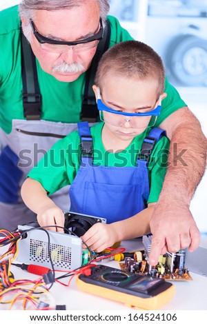 Grandfather teaching grandchild measuring with digital multimeter on disassembled PC power supply