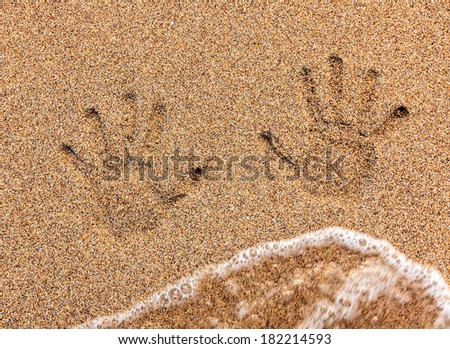 Child handprint on sand being washed away by sea wave