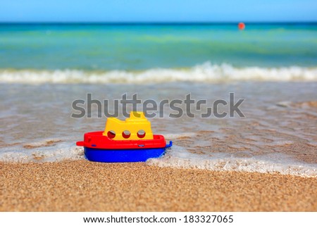 Little toy ship on beach awash by waves