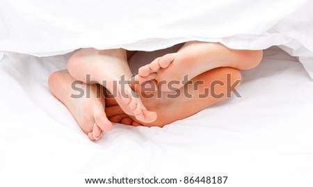 Man and women feet hanging out from under white quilt