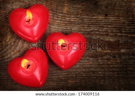 Three candles in shape of heart on old wooden background