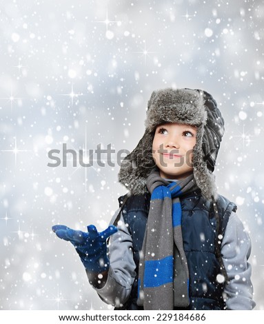 Winter fur hat clothing boy with outstretched hand and looking snow falling