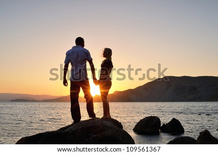 Young boy and girl look at each other, hand in hand on the beach at sunset