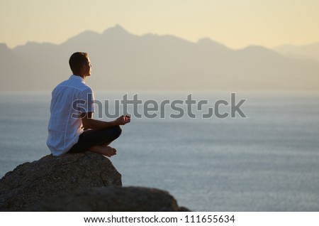 Guy sitting on a rock in the lotus position and looking at the setting sun