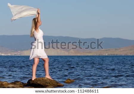 Girl stands on a rock in a white dress with a white scarf