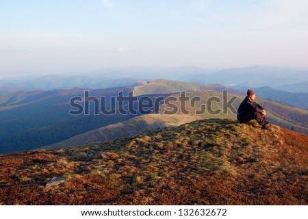 Man in black jacket sitting on top of a mountain and looks into the distance