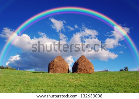 Summer mountain village landscape with a rainbow over haystacks