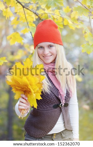 Happy young blond woman smiling and offering a bouquet of yellow autumn leaves