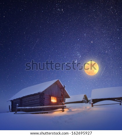Winter landscape with a starry sky and the full moon. The light in the cabin in the mountains