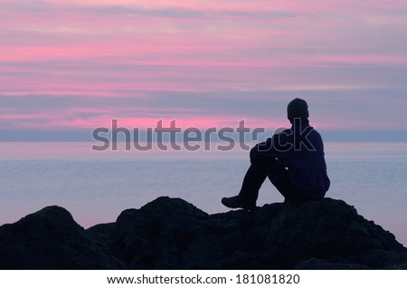 Evening at the seaside. Guy sits on a rock by the sea and looking at sunset