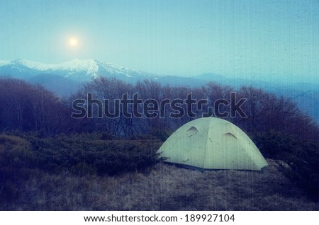 Spring landscape at night. Camping in the mountains in the moonlight. Tent in the mountains. Carpathians, Ukraine, Europe. Filtered image: vintage, grunge and texture effects