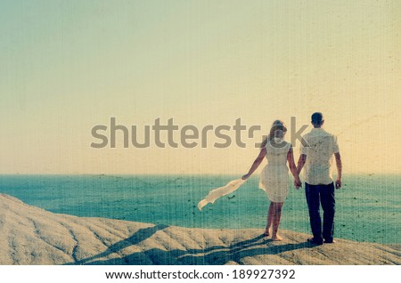 Loving couple looking at the sea holding hands. Filtered image: vintage, grunge and texture effects
