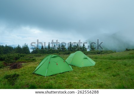 Camping in the mountains. Two green tourist tents. Evening landscape with cloudy sky.