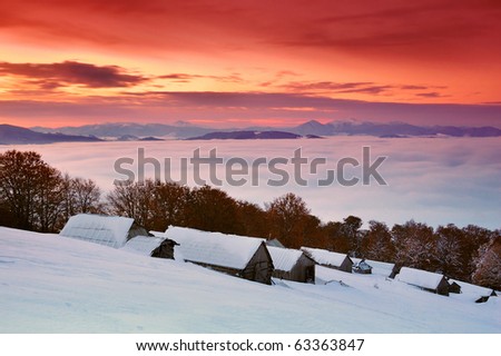 Sunrise in a mountain valley with huts and the first snow in October