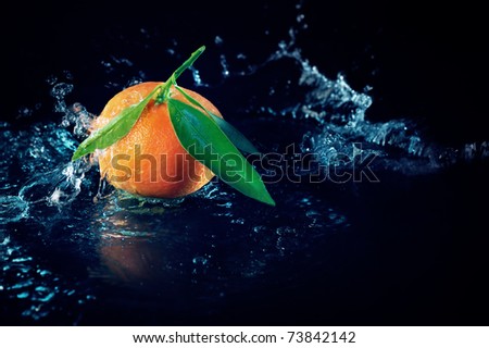 Ripe orange with leaves on a black background with water splashes