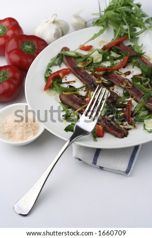Finely sliced raw bleu beef with rocket and baby capsicum. Condiments of Murray River pink salt flakes and soy. Baby capsicum or peppers and garlic on a ceramic plate.