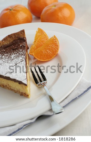 An angle view of a slice of chocolate mocha and orange cheesecake. Table setting with dessert fork and mandarin oranges for styling. Focus point on fork and top of cheesecake.