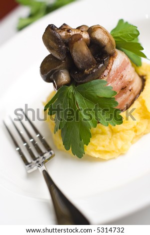 Lamb wrapped in bacon served with button mushrooms on butter pumpkin and potato mash. Garnished with flat leaf parsley.