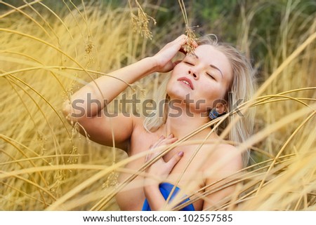 Portrait of a beautiful woman topless blonde, who straightens her hair in the dry reeds