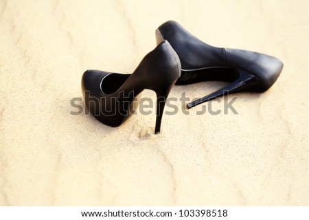 Black women\'s high heels are in the sand on a sunny summer day, isolated