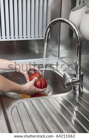 Girl\'s hands washing red tomatoes in the kitchen sink