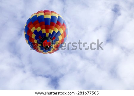 Underneath view of a single hot air balloon rising up to a blue sky full of clouds