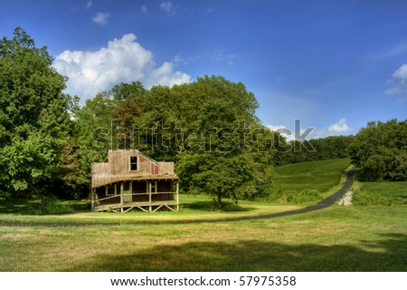 Old abandoned rustic house, green hill and trees, with blue sky and white clouds